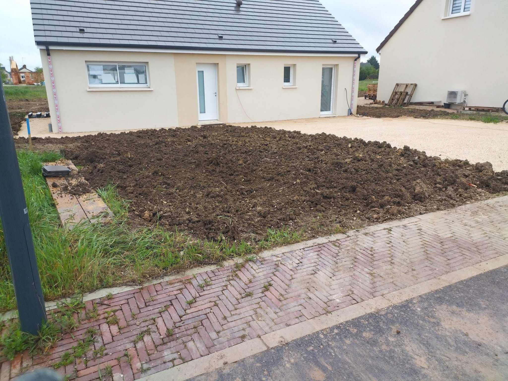 Terre fraîchement travaillée devant une maison neuve, prête pour l’engazonnement, avec allée gravillonnée et pavé en premier plan.